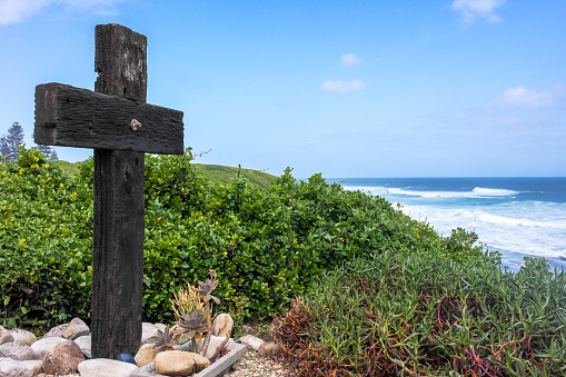 Jesus Christ cross. Easter, resurrection concept. Christian wooden cross on a seascape background with sea plants and shrubs overlooking the southern ocean