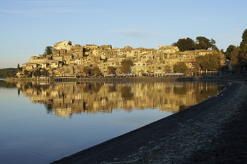 the historic center of Anguillara Sabazia, is reflected in the Bracciano lake, illuminated by the light of the sunset