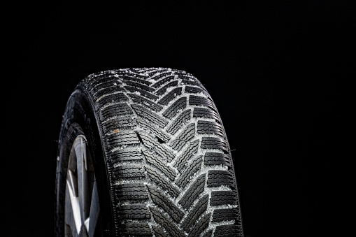 Close-up of snow on new car tyre against black background.