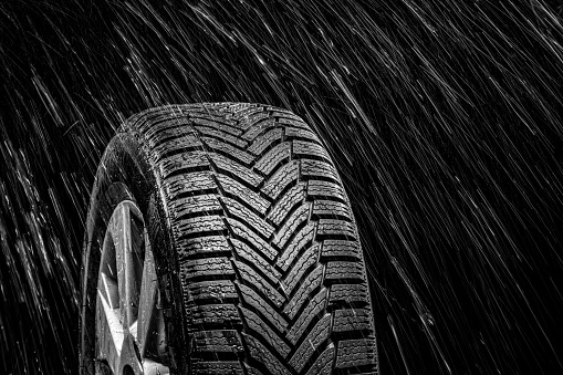 Close-up of water falling on new car tyre against black background.