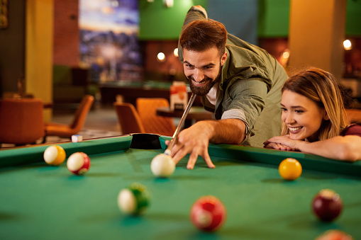 Young happy couple enjoying playing billiard together in pool hall