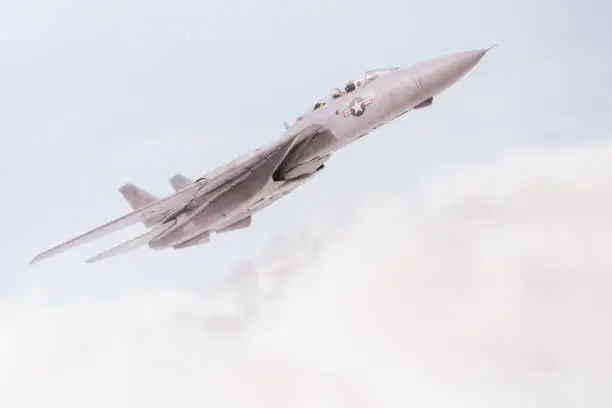 An F14 Tomcat streaks through the sky, high above the clouds. Scale model photography
