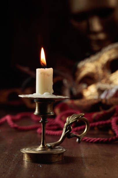 istock Burning candle in an old brass candlestick and carnival masks. 1442174014