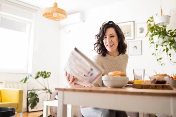 istock Young woman having breakfast at home looking at newspaper 1442177687