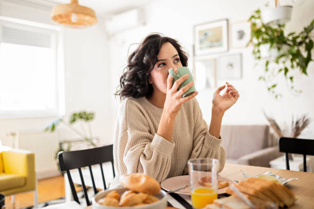 young woman having breakfast at home drinking coffee - waffle breakfast food sweet food imagens e fotografias de stock