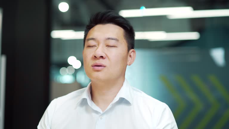 Asian business man meditating. Successful businessman meditates sitting at table in modern office, relaxes, after working on laptop