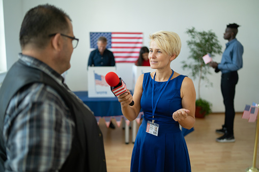 A female journalist is talking to a local man on Election Day in the polling center
