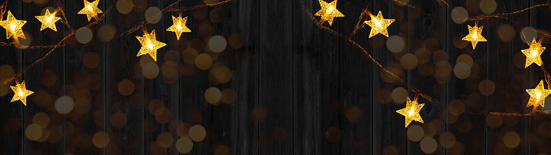 Chrsitmas celebration decoration background banner panorama - Golden star light chain hanging on dark black wooden boards wall texture
