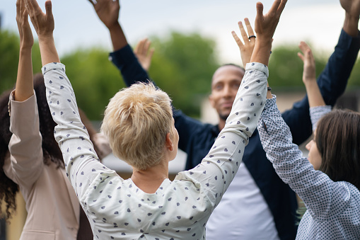 A diverse mixed group of patients celebrating with their arms in the air during an outdoor therapy meeting