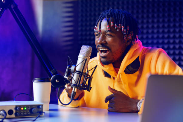 African radio host sitting at desk recording in studio with microphone and laptop African radio host sitting at desk recording in studio with microphone and laptop close up radio dj stock pictures, royalty-free photos & images