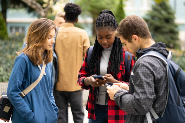 studenti multietnici che usano i loro smartphone mentre escono dopo le lezioni - untucked foto e immagini stock