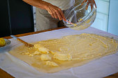View of a woman putting chasse over batter on rolled dough in process of making apple strudel, pie at her home.