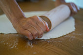 View of a woman rolling dough on desk in process of making apple strudel, pie at her home.