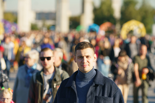 Moscow, Russia - September 10, 2022: Portrait of young man on the city street in autumn day. Lifestyle concept. Front view. Defocused crowd people as background. Concept of the individuality