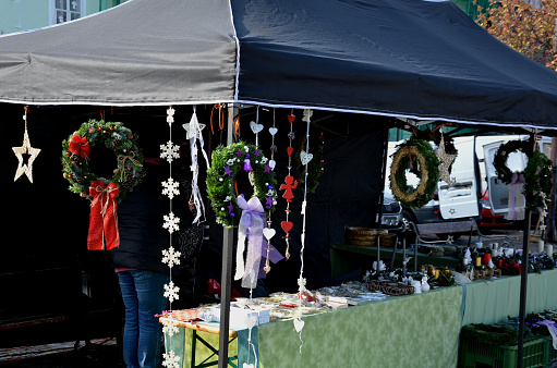 marketplace with Christmas decorations, handicrafts in a stall on  square. a tent on which structure hangs exposed decorative wreaths for graves with an Advent theme made of moss. ribbons and candles