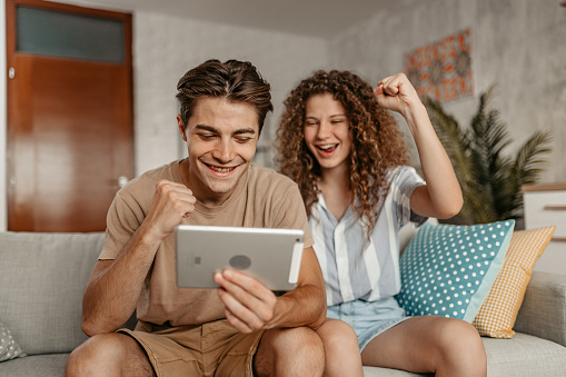 Beautiful young happy couple rooting for their team while watching the game on a digital tablet. Scoring in the game.