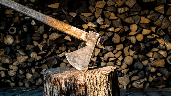 A wooden-handled sharp axe stuck in a wooden stump in the middle of a dry grass field under the cloudy sky
