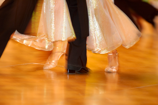 Dancing woman's feet in glossy pink sandals on orange floor with one man's foot in between