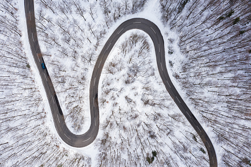 aerial view, drone point of view directly above cury road through forest on cold winter day with snow