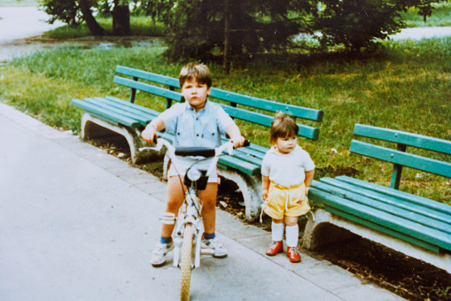 Baby brother and sister have fun in public park at eighties
