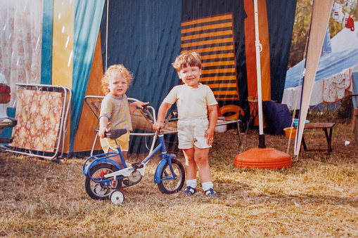 Brother and sister posing by bicycle in camp at eighties