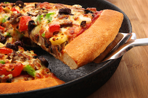 A slice of hot, fresh pizza being served. Narrow DOF focus on slice toppings