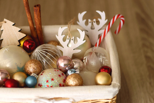 Wicker basket filled with various colorful Christmas decorations on wooden table. Selective focus.