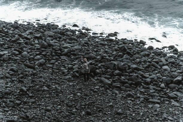 A lonely woman on a cloudy day stands on a black pebble beach in Ribeira da Janela, Madeira.