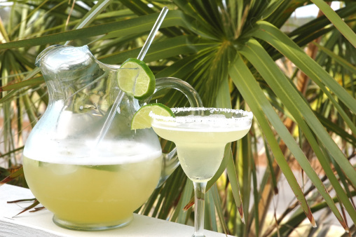 Margarita with salt and lime with pitcher and palm tree in background.
