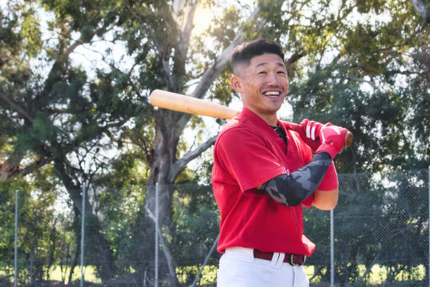 młody azjata trzymający kij baseballowy stojący na boisku i uśmiechnięty - baseball player baseball holding bat zdjęcia i obrazy z banku zdjęć