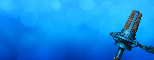 istock Professional studio microphone on blue background with spotlights bokeh and copy space for podcast banner, broadcast radio website or music event title background. 1442231146