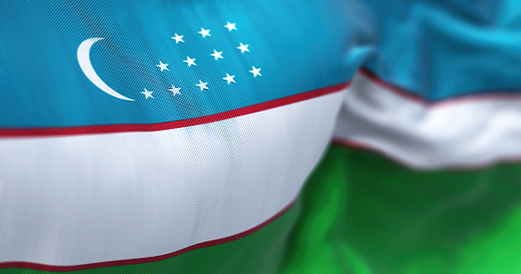Close up view of the Uzbekistan national flag waving in the wind. The Republic of Uzbekistan is a country located in Central Asia. Fabric textured background. Selective focus. 3D illustration