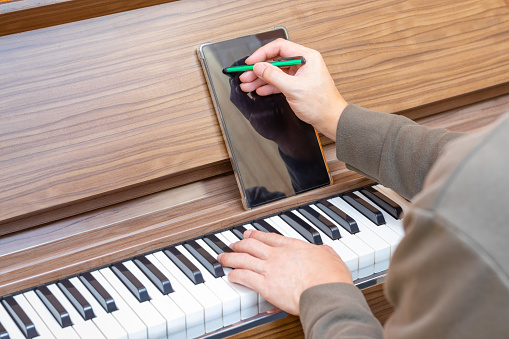 closeup male musician, songwriter hand writing hit song on tablet computer while playing acoustic piano. songwriting concept