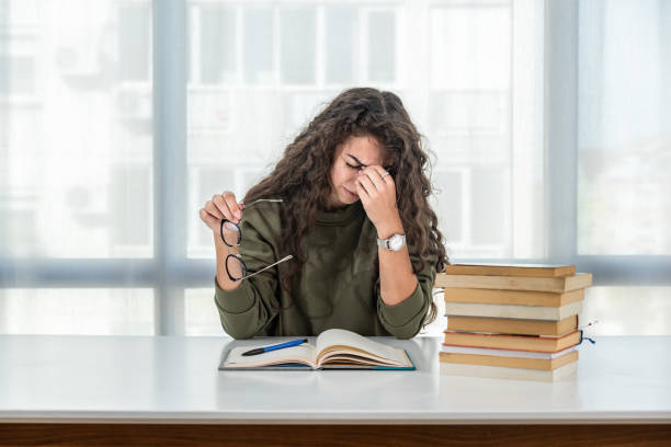 junge teenager-schule oder college-universität mädchen mit lockigem haar haben kopfschmerzen und ist müde nach stunden des lesens von büchern und lernen für die bildungsprüfung. angst- und wunde-augen-konzept. - schoolgirl boredom frustration adult student stock-fotos und bilder