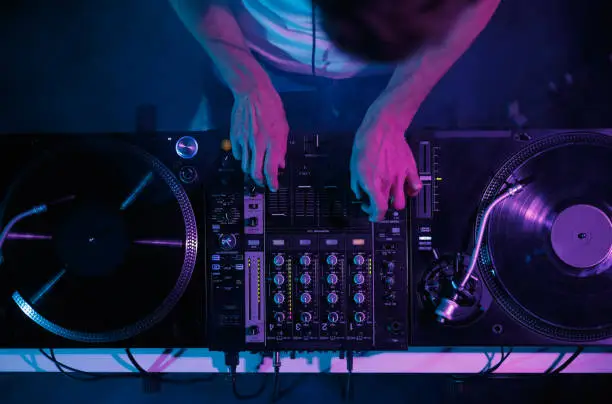 Photo of Hip hop dj plays music on concert. Disc jockey mixing musical tracks with vinyl turntables and sound mixer in night club