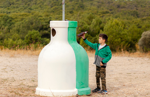 View of a child throwing glass bottles in recycling bin.