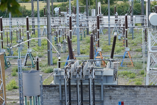 High voltage electricity power distribution plant and electricity pillars with ceramic insulator and a lot of cables and wires as a part of hydro power plant during sunny day.