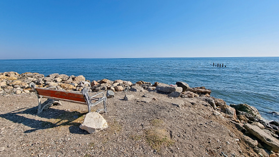 a bench standing alone on the shores of the Mediterranean Sea, looking into the distance to sit alone. Romantic place for lovers.