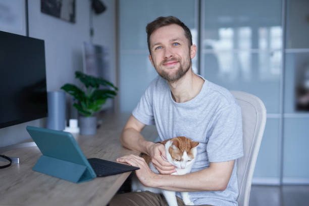 istock Young caucasian man with his cat using tablet at home office, looking at camera 1442247757