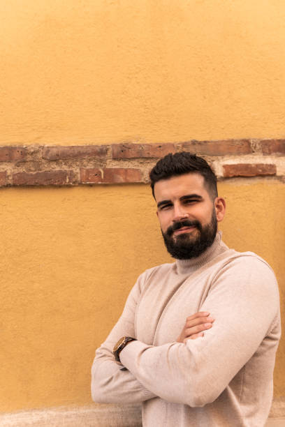 istock Vertical image of a laughing young man with beard and collared sweater looking at camera with crossed arms and confident airs. 1442250538