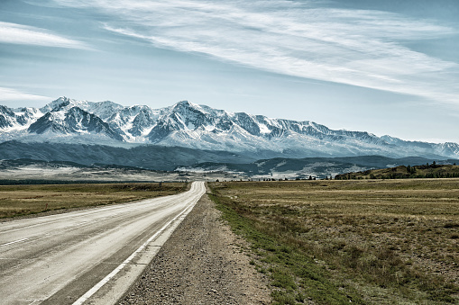 Straight asphalt road goes to the mountains range with the snow on the top. Toned landscape image