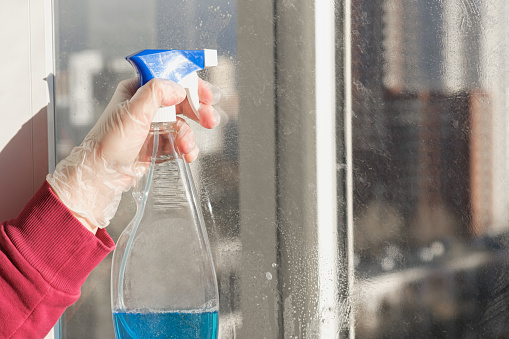 Woman's hand in a rubber glove holding spray bottle for cleaning windows. Window cleaning tools. Concept of cleaning company services, window cleaning, housework.