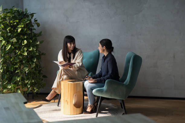 colegas amigables sentados en sillones disfrutan de la charla en el espacio de la oficina - interview meeting business women fotografías e imágenes de stock