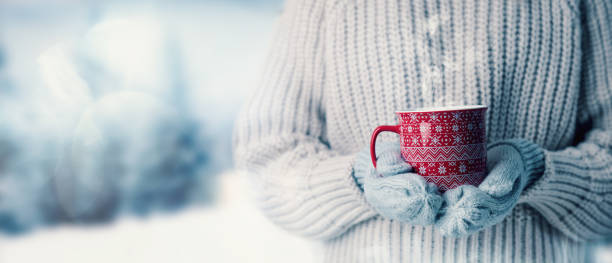 woman in wool sweater and mitten gloves holding a cup of hot steaming drink on snowy winter landscape background. banner with copy space - glove winter wool touching imagens e fotografias de stock