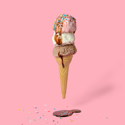 funny creative concept of flying wafer cone with ice cream covered, strewed sprinkles and poured with chocolate icing on pink background