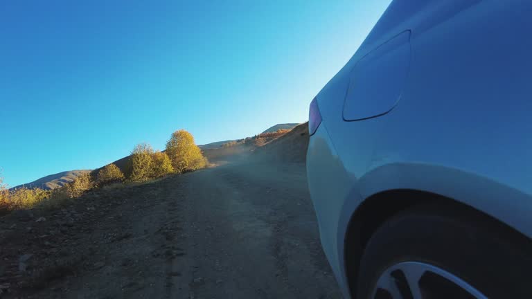 Car wheel spinning on mountain dusty road and sunset lights streaming POV