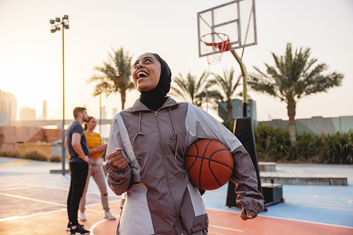 Middle Eastern Female Standing And Looking Up Laughing In Front Of A Camera Laughing While Holding The Ball Outdoors In Dubai.
