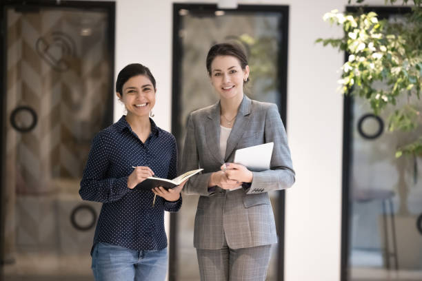 istock Two attractive multiethnic businesswomen looking at camera pose at workspace 1442259727