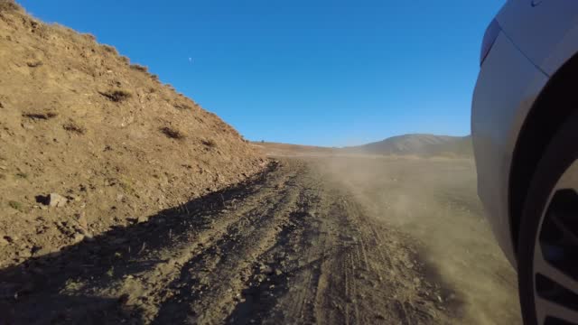 Car wheel spinning on mountain dusty road and sunset lights streaming POV