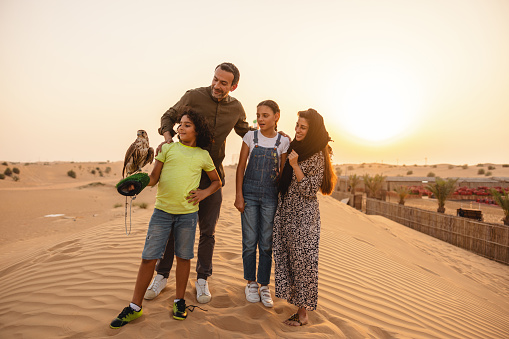 Middle Eastern family outdoors at sunset in Dubai Desert holding a trained falcon.
